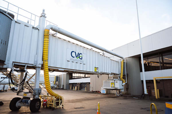 A photo of a white jet bridge extending from the airport. The CVG logo, consisting of the CVG letters in blue with a green swoosh going through the letters up to the right, is visible on the side.