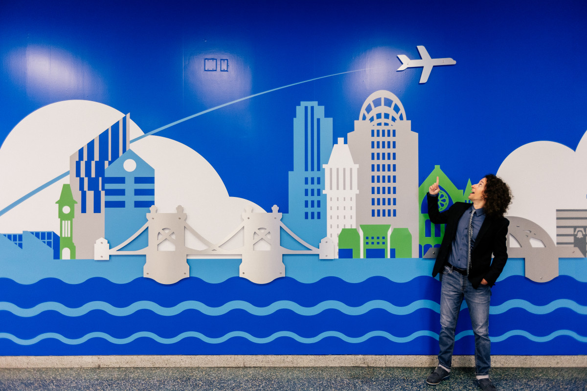 A photo of Jay Kruz in front of a blue wall at CVG that showcases the Cincinnati and Northern Kentucky skyline.