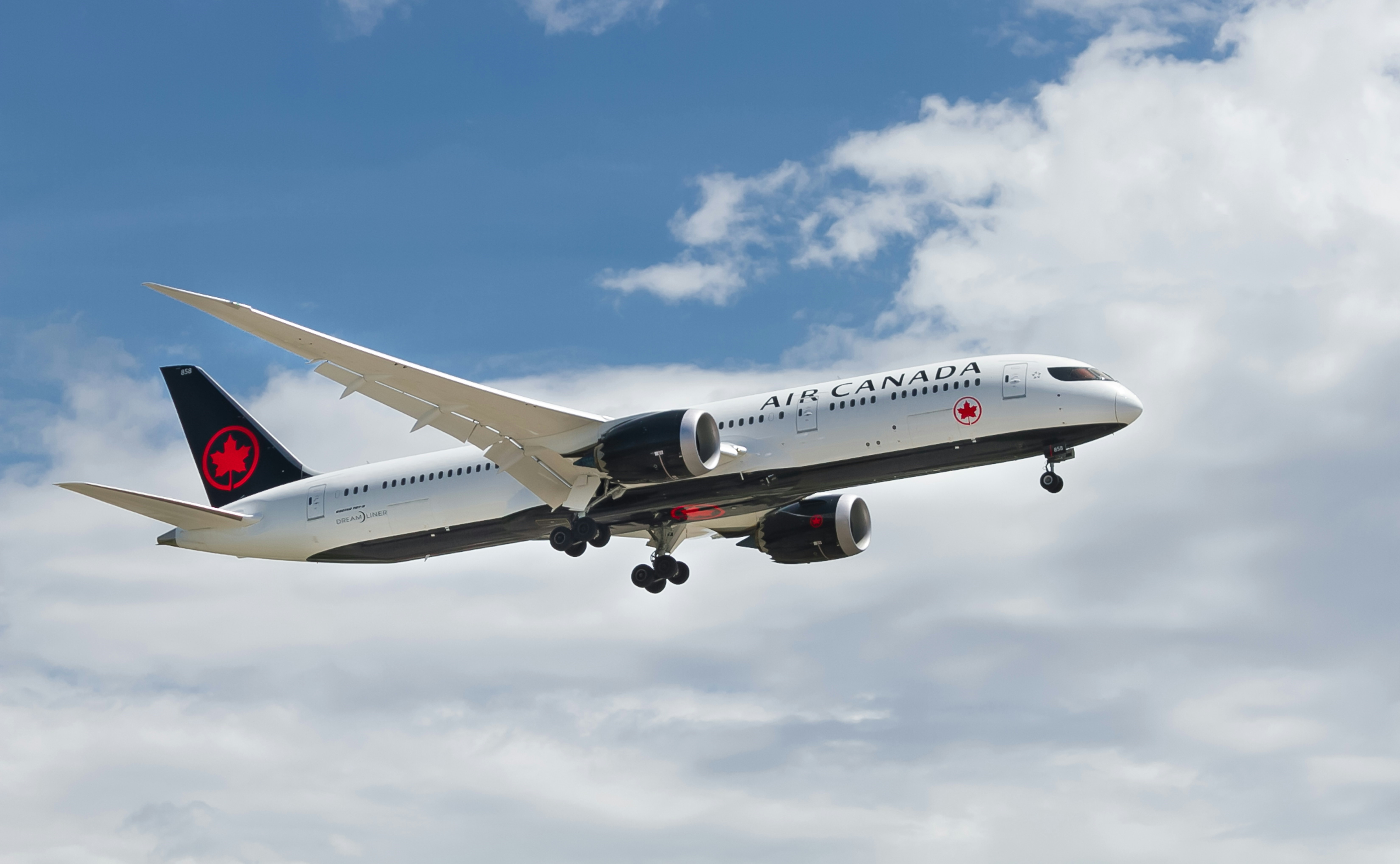 A photo of an Air Canada plane flying in a bright blue sky with clouds.