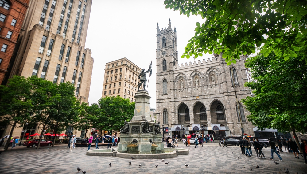 A photo of Montreal, Quebec, Canada that showcases a fountain and large buildings along a cobblestone street.