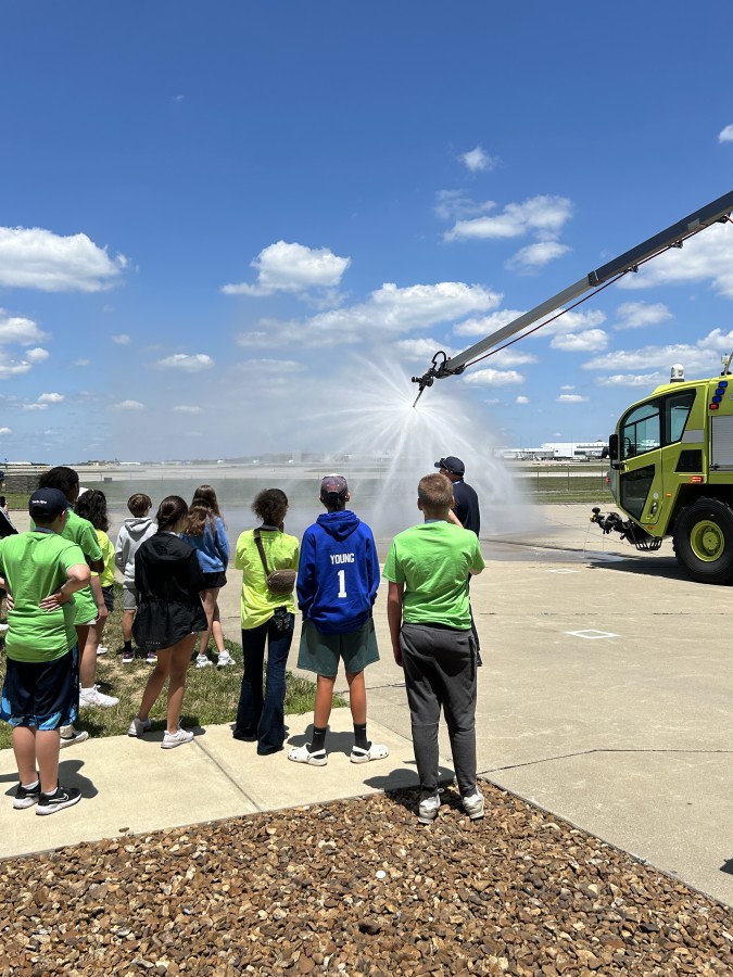 A photo of students touring ARFF and watching the fire truck spray water.