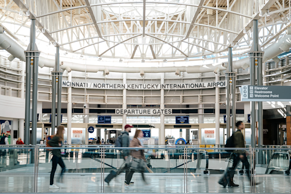A photo of passengers walking across the Ticketing Bridge with the TSA Checkpoint and the words Cincinnati/Northern Kentucky International Airport in the background.