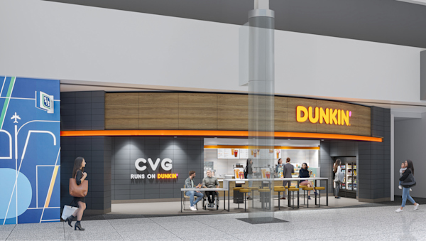 A rendering of the new Dunkin' location in CVG. The building has dark gray on the walls with a sign that reads "CVG runs on Dunkin'". On the top of the build out, there is wood paneling with a bright orange bottom border and the sign in orange reading "Dunkin'".