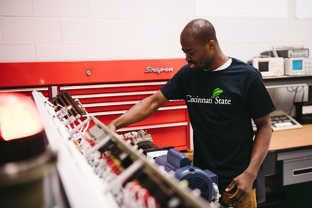 A photo of a man wearing a Cincinnati State t-shirt standing in front of a large red toolbox.