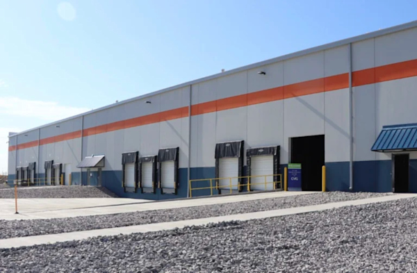 A photo of the side of a cargo facility with open dock doors. There is an orange stripe running along the top of the building. It is a sunny day with a clear blue sky.