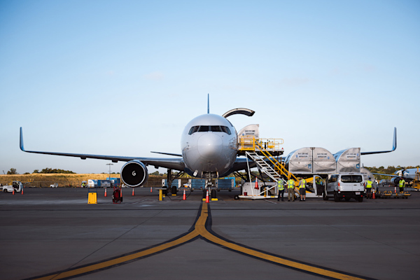 A front photo of an Amazon Prime Air plane being loaded with cargo on a sunny day with a bright blue and cloudless sky.