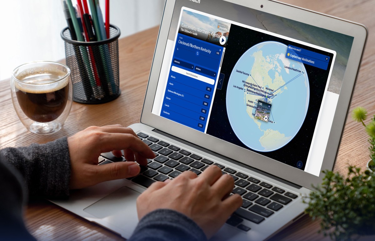 A photo of a person sitting down at a laptop, only their hands and wrist visible as they type on a computer that has Voyager pulled up on it. There are pens and a cup of coffee beside them on the desk.