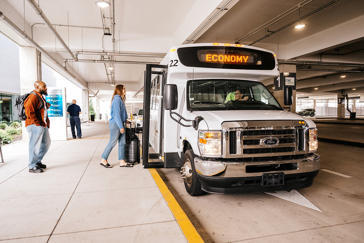 A photo of a white shuttle that says Economy on the digital sign on top is picking a male and female up in a parking garage structure.