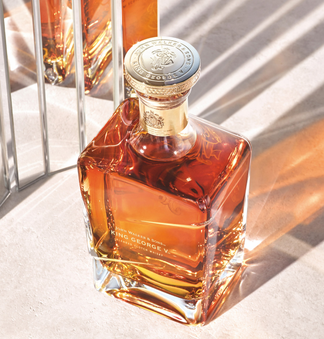 A close-up, top-down shot of a bottle of John Walker & Sons King George V Blended Scotch Whisky, with a soft reflective/ mirror-like background. 