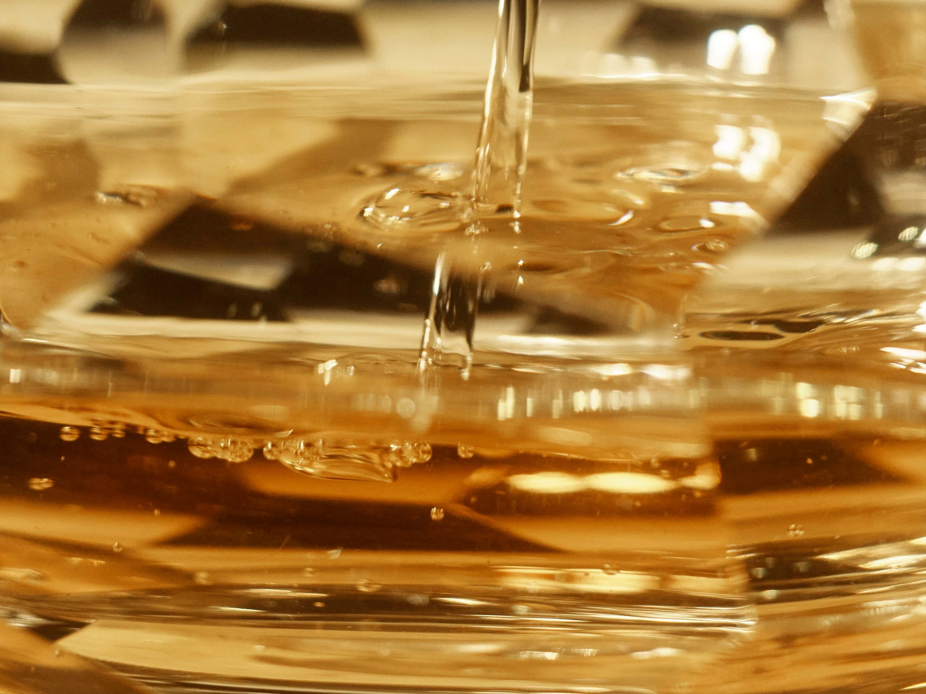 A close-up of tequila poured, capturing the golden liquid as it flows and creates bubbles on the surface. 