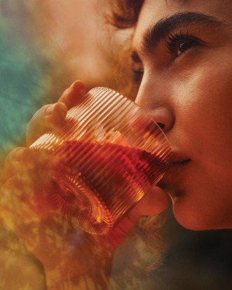 A close-up of a person sipping from a textured glass filled with an amber-colored drink. 