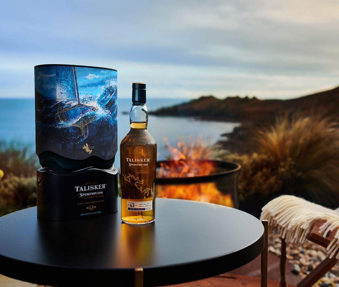A bottle of Talisker Xpedition Oak 43-year-old single malt Scotch whisky sits on a round table next to its ocean-themed box