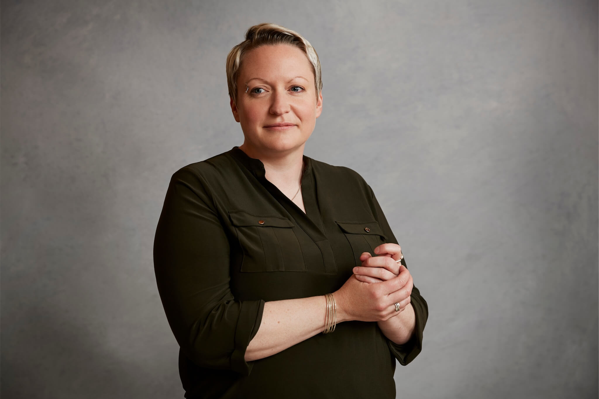 A portrait of Emma Walker, wearing a dark green blouse, with her hands clasped together in front of her.