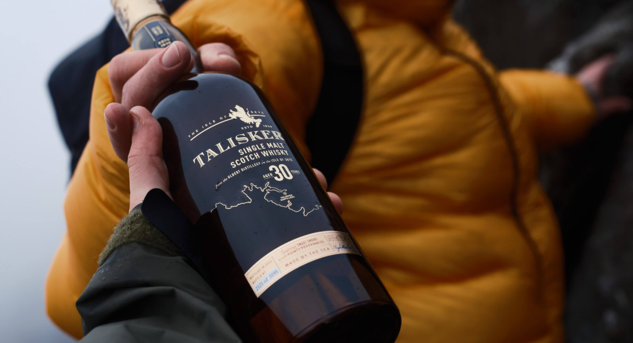 The image shows a person holding a bottle of Talisker 30-Year-Old Single Malt Scotch Whisky