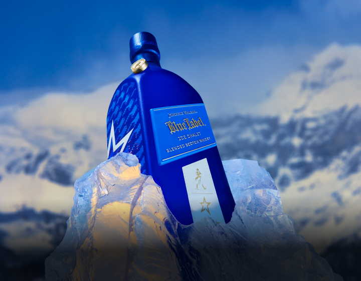 An elegant blue bottle of Johnnie Walker Blue Label sits atop a crystal-clear ice sculpture, showcasing a bold houndstooth pattern 