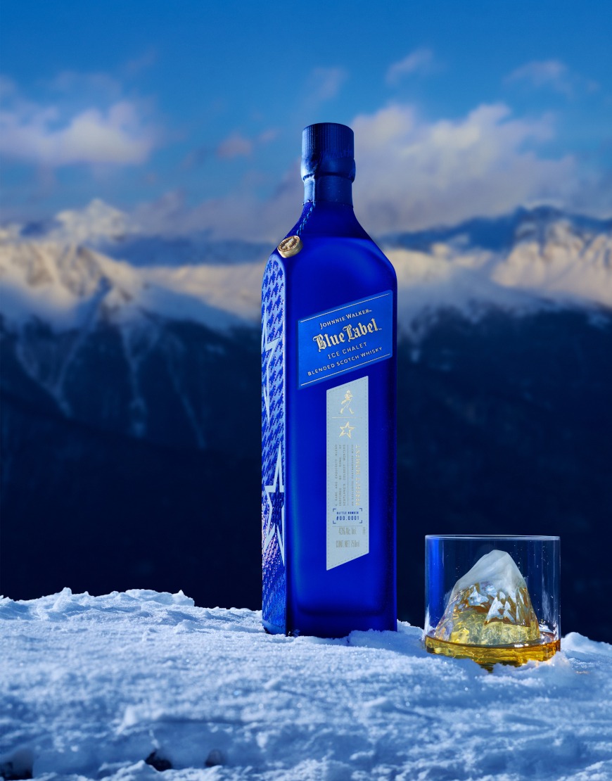 A striking blue bottle of Johnnie Walker Blue Label Ice Chalet stands elegantly on a snow-covered surface with a mountainous backdrop