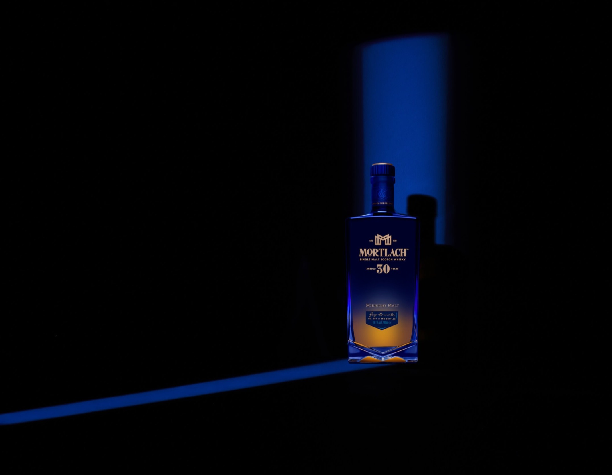 A bottle of Mortlach 30-year-old single malt Scotch whisky stands illuminated against a dark