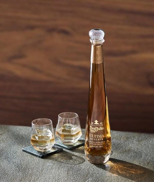 A tall, elegant bottle of Don Julio Última Reserva Tequila is placed on a grey textured surface