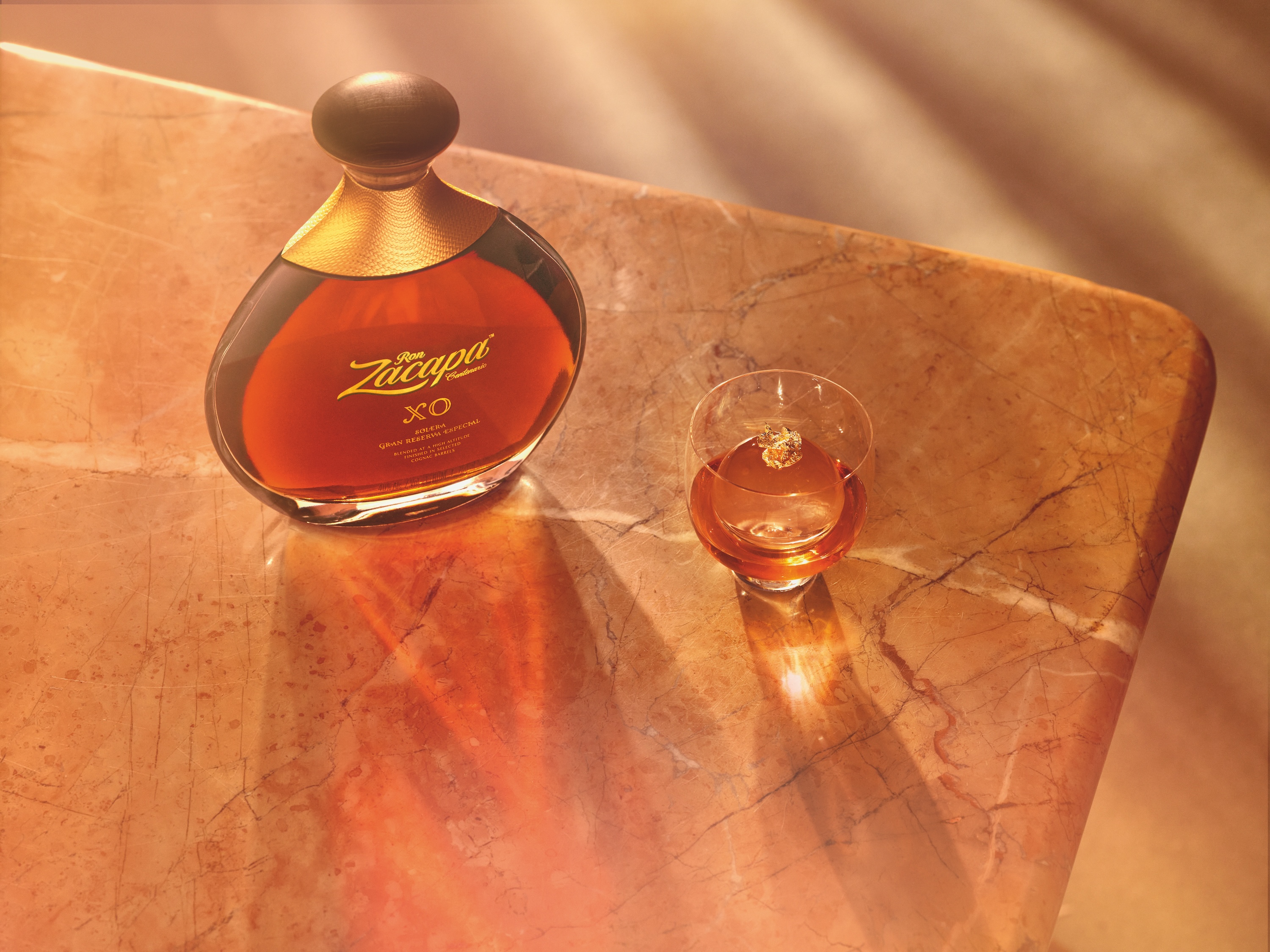 A bottle of Ron Zacapa XO with its rich amber liquid and gold detailing sits elegantly on a warm