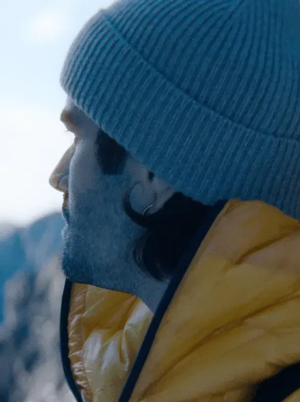 The image shows a person in a side profile, wearing a gray knit beanie and a yellow puffer jacket