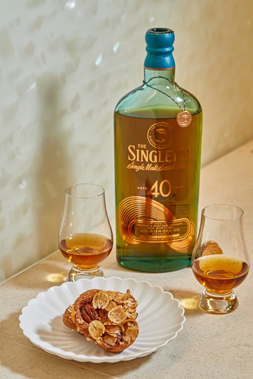 A bottle of The Singleton 40-Year-Old Single Malt Scotch Whisky is placed on a countertop, flanked by two whisky glasses filled with amber liquid. 