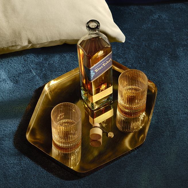 Johnnie Walker Blue Label on a table with two glasses of whiskies on either side of the bottle