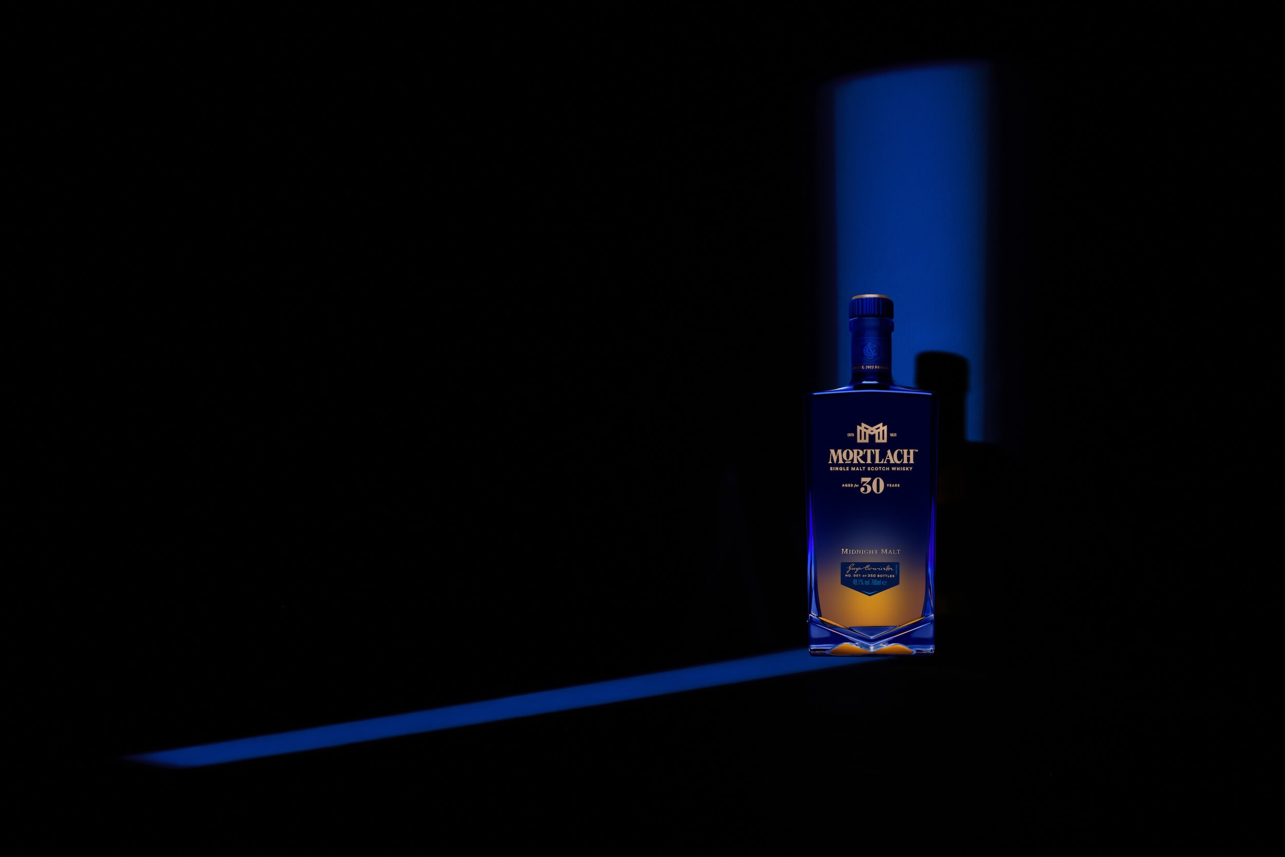 A bottle of Mortlach 30-year-old single malt Scotch whisky stands illuminated against a dark