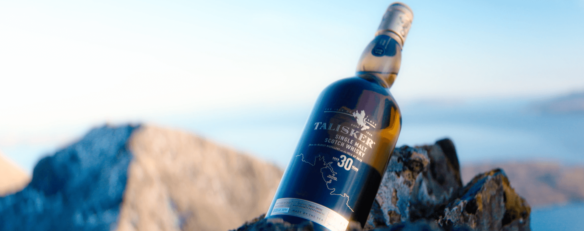 The image shows a bottle of Talisker 30-Year-Old Single Malt Scotch Whisky lying slanted on a rugged rock