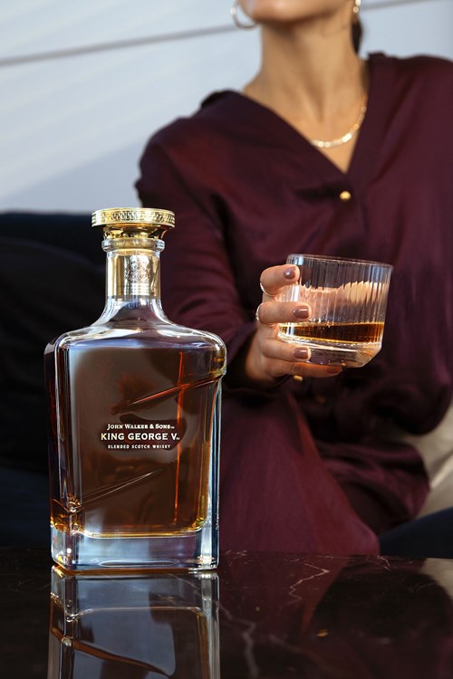 The image displays a bottle of John Walker & Sons King George V Blended Scotch Whisky on a glossy black marble surface,