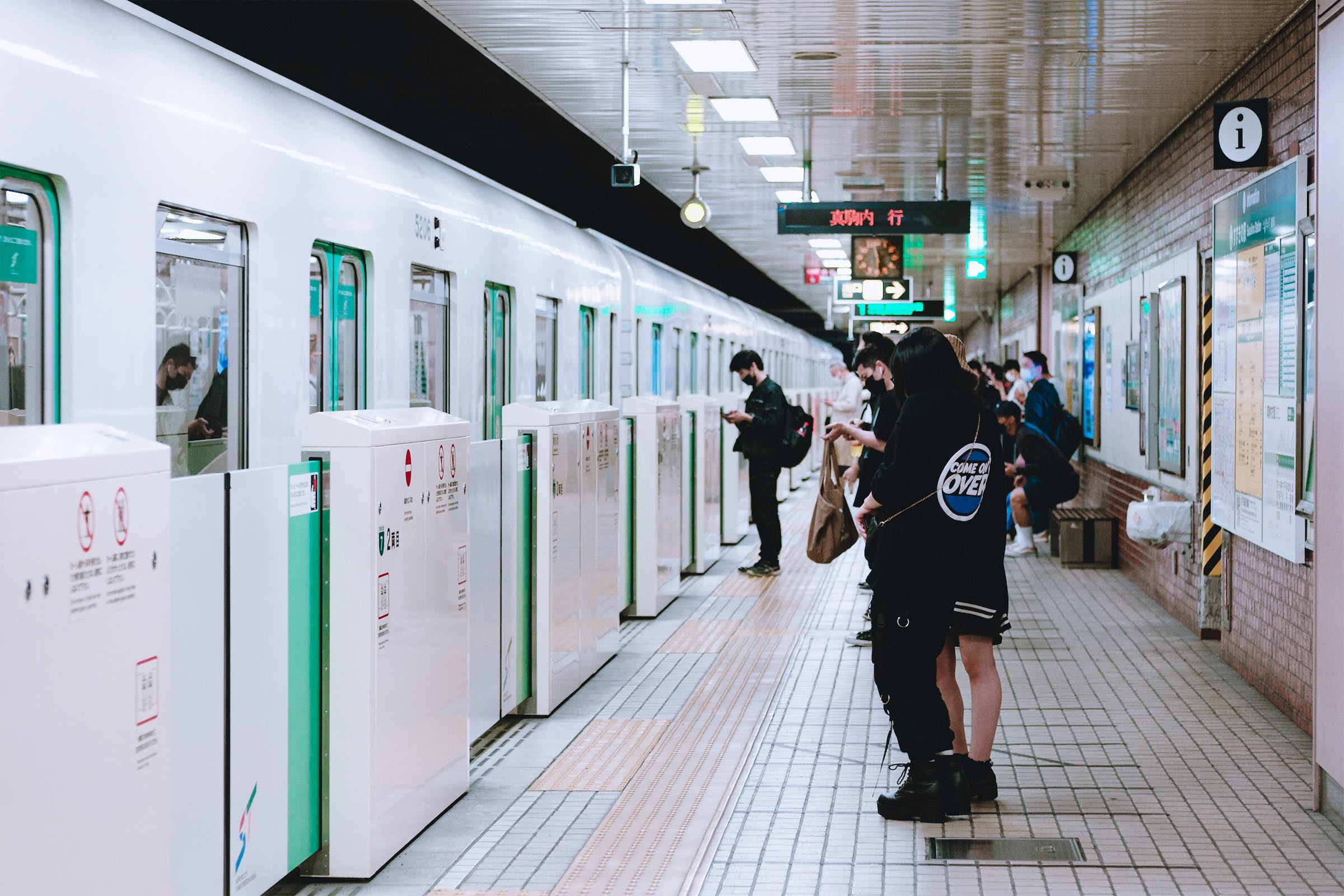 A crowd of people wait on a subway platform in Susukuno, Sapporo. A train has just arrived and is pulling up to the automatic gates.