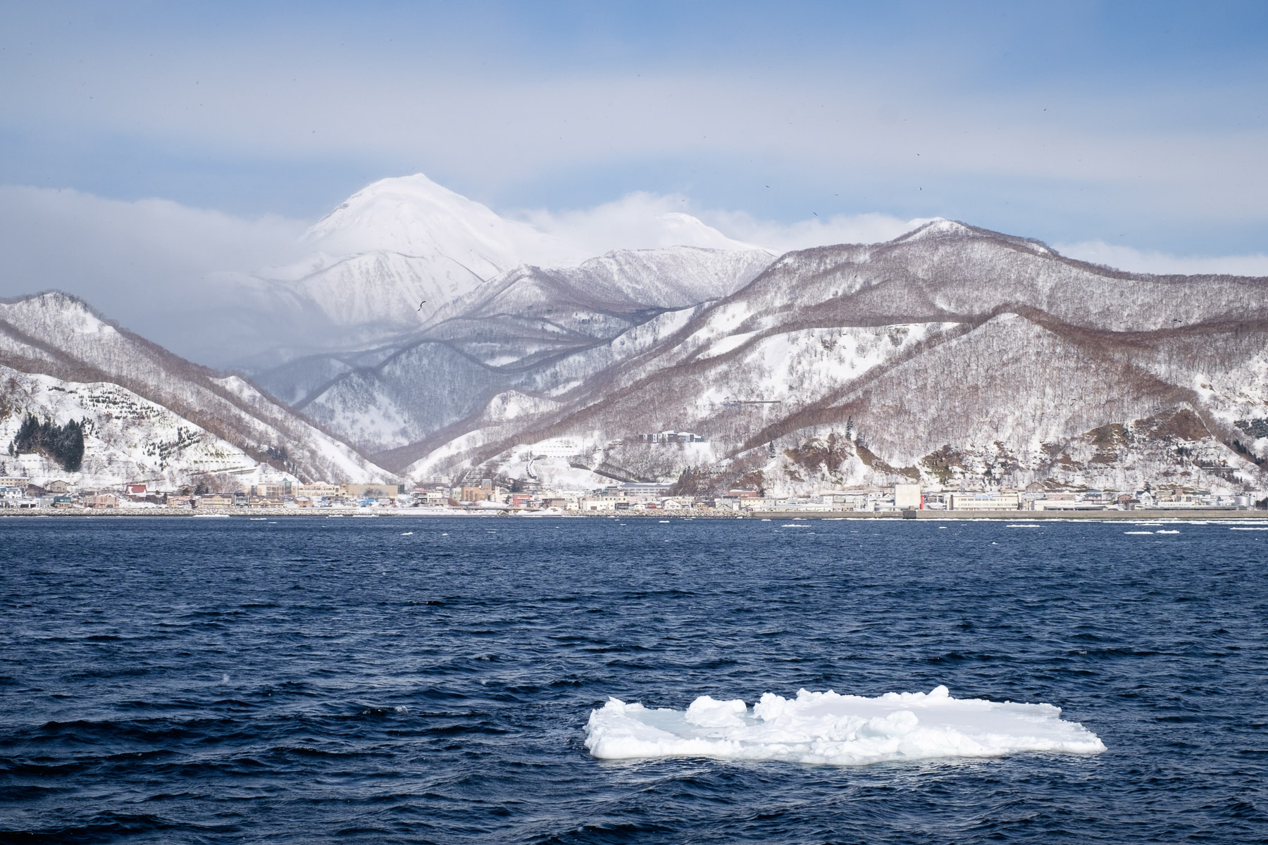 Mt Rausu, seen from the sea, rises above Rausu town. In the foreground a lone patch of drift ice floats past.