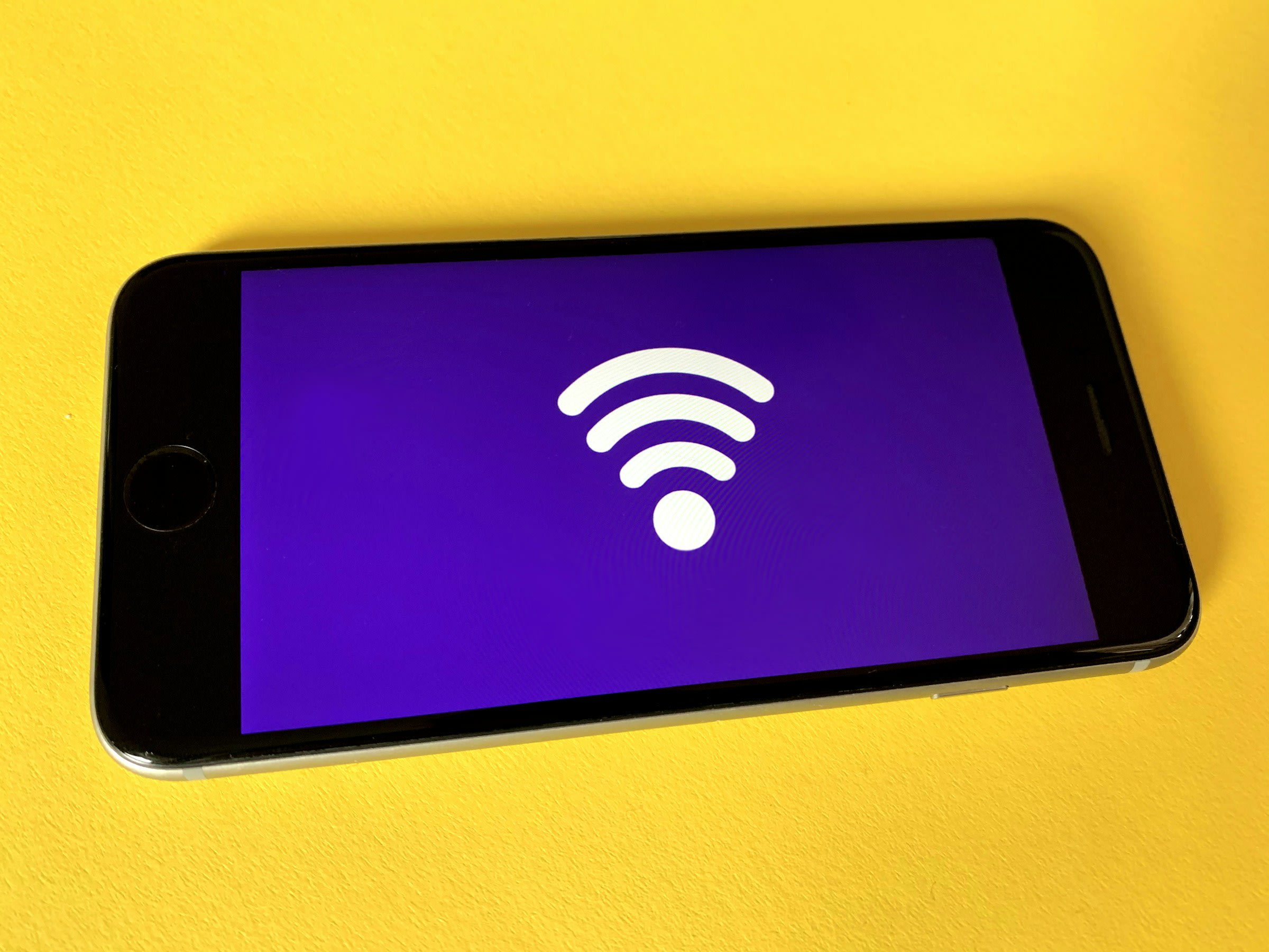 An image of a smartphone with a WiFi symbol on its screen on a yellow surface.
