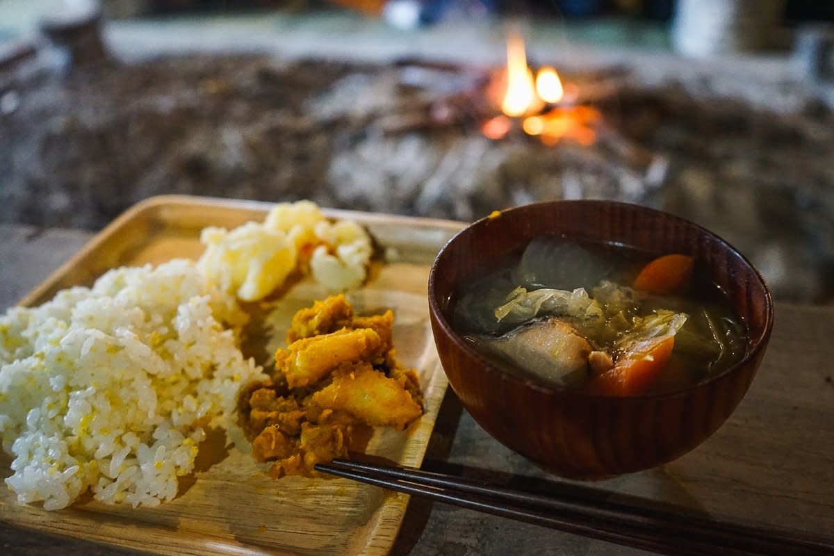 A meal featuring traditional Ainu ingredients sits on a bench in front of a fire