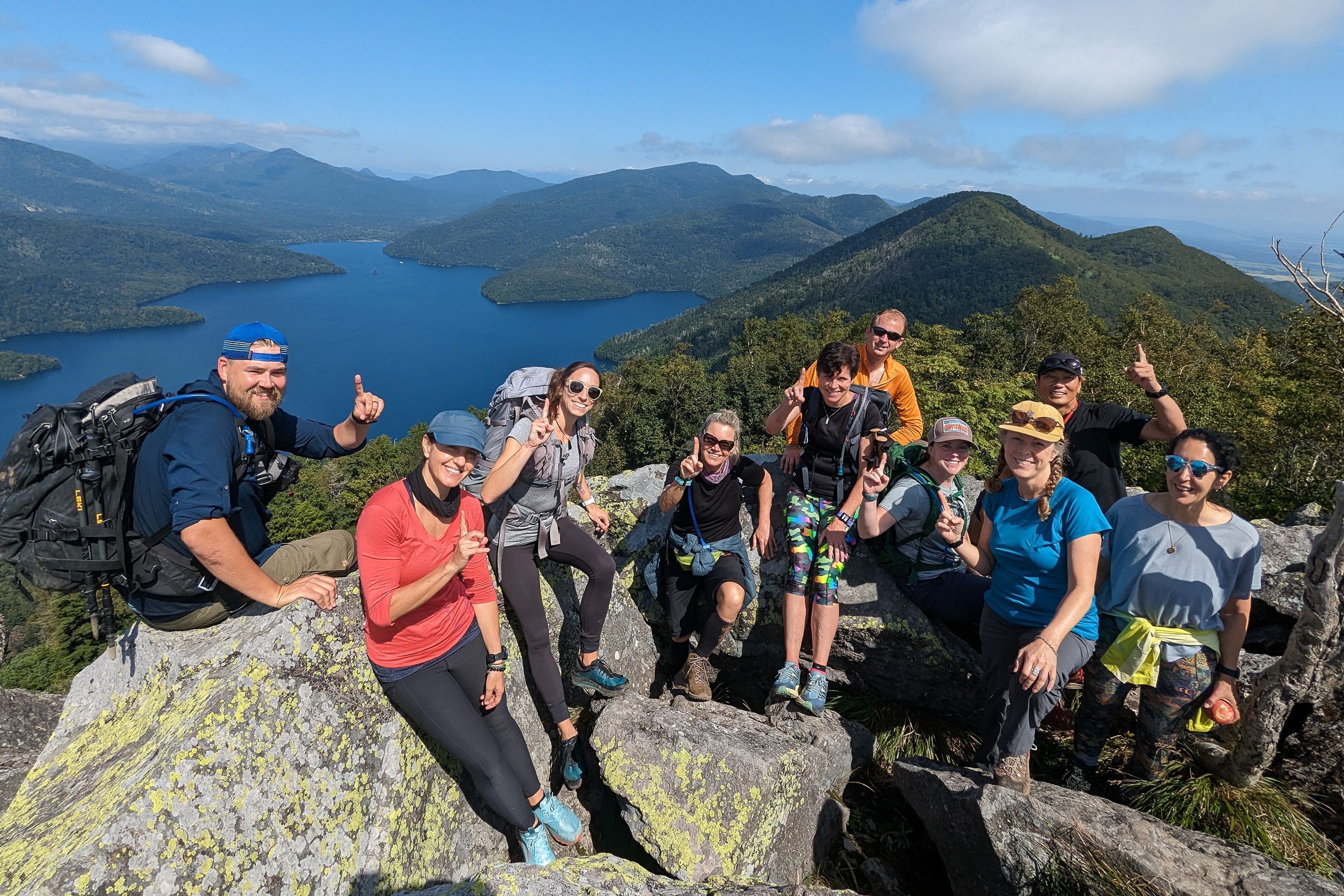A group of hikers pose triumphantly at the peak of Mt. Hakuunzan on a sunny day.