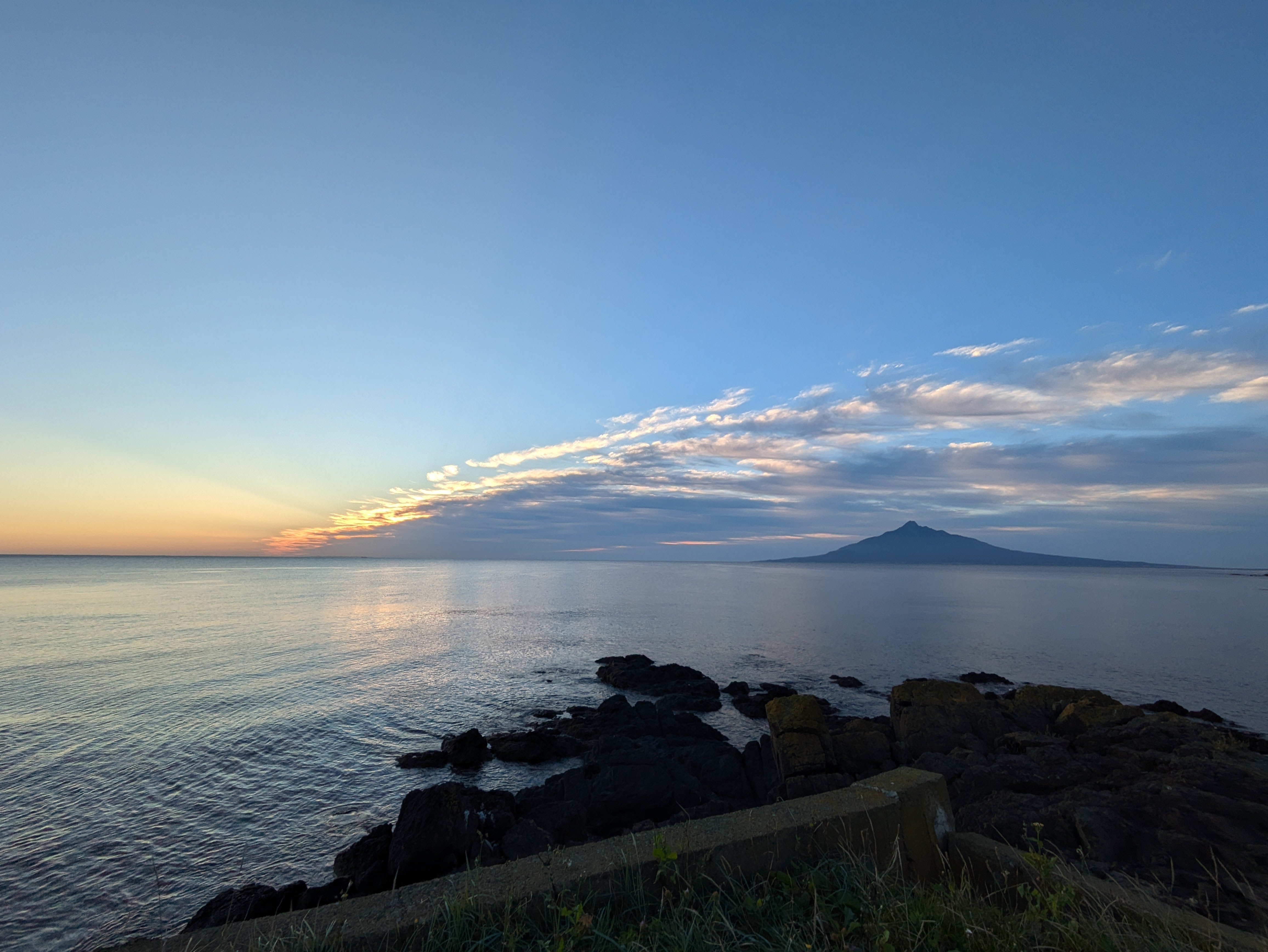 A view of Mt. Rishiri as seen from Rebun Island in the evening. The sun is setting and the ocean is visible un the foreground.