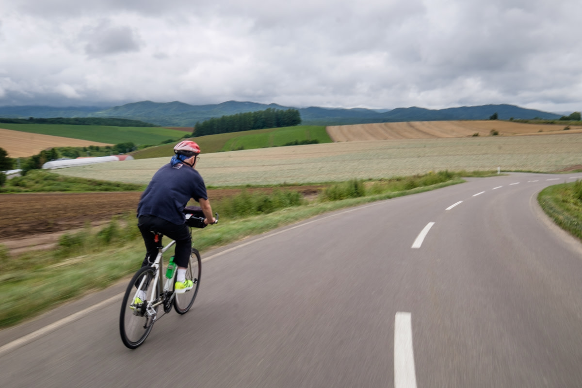 A cyclist speeds down a quite road surrounded by farmland