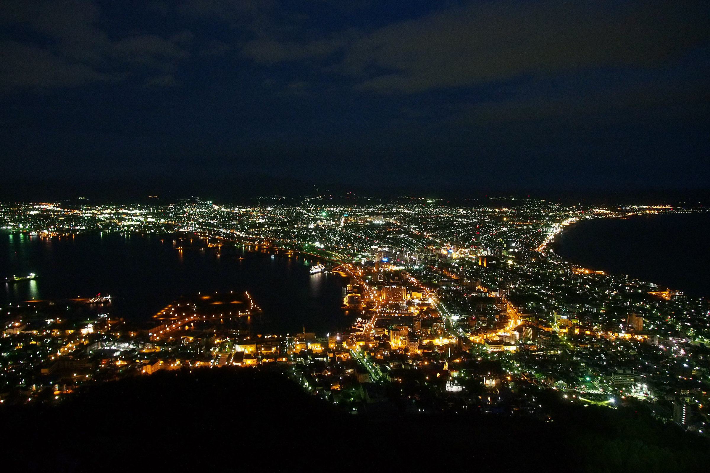 A night view of Hakodate. It is dark but the city below is lit up brightly.