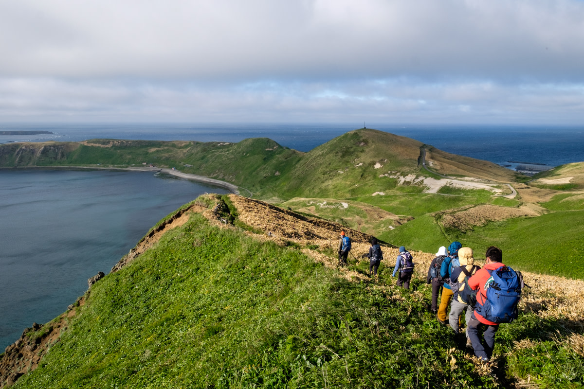A group of hikers walk along a windswept ridge looking over the Sea of Japan on Rebun island