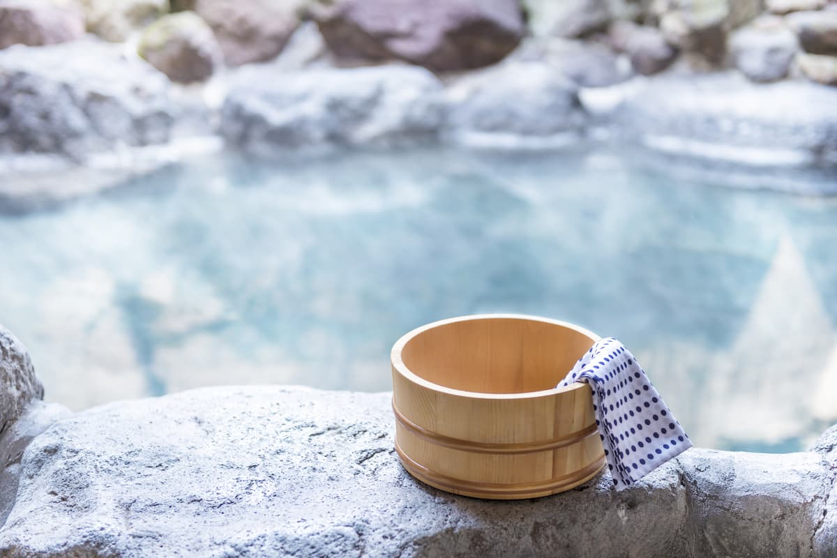 A small towel hangs out of a wooden bowl that is placed on the edge of an onsen hot spring pool.