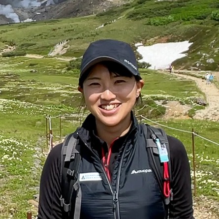 Adventure Hokkaido guide Yuka smiles at the camera while standing in an alpine meadow full of wild flowers.
