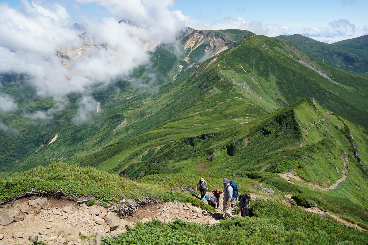 A group of hikers climbs Mt. Furano, with Mt. Tokachi in the background