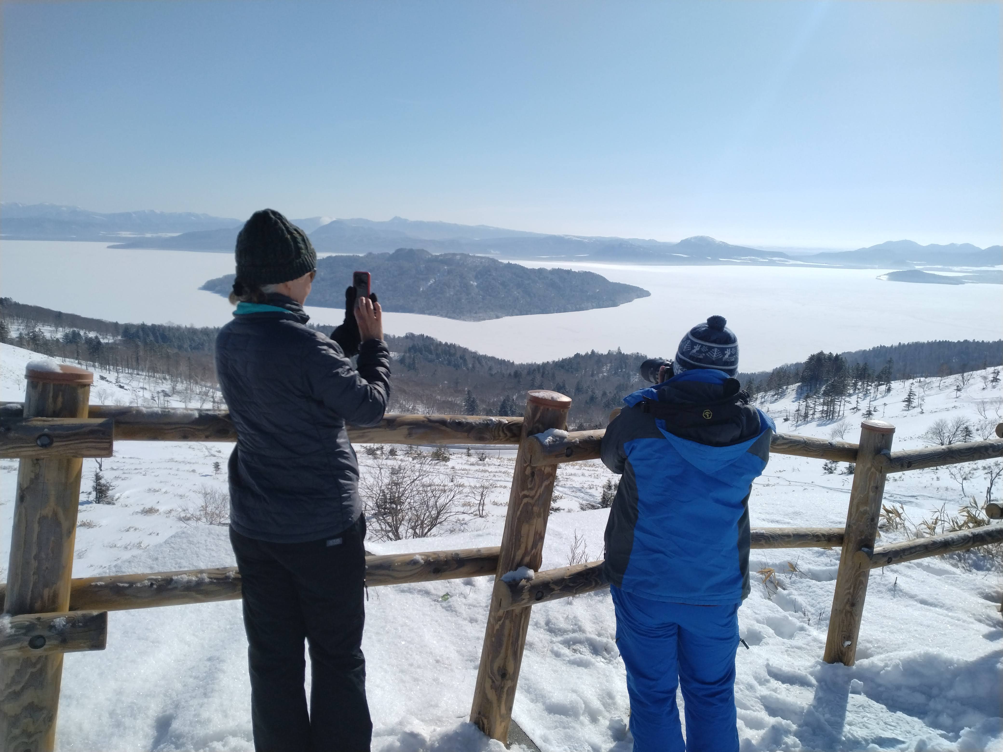 Two guests take pictures of a frozen Lake Kussharo from Bihoro Pass's lookout point.