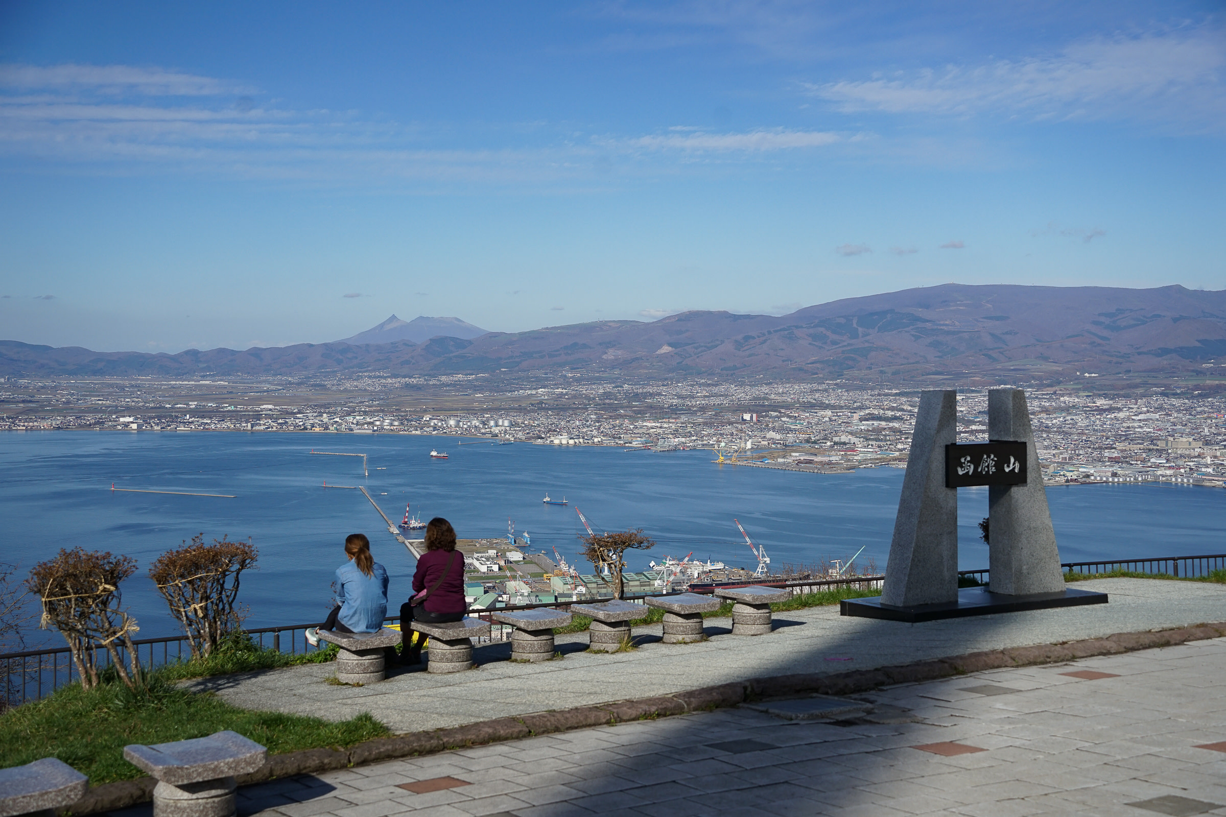 Two girls sit at the top of Mt. Hakodate looking out over Hakodate city and Hakodate Bay.