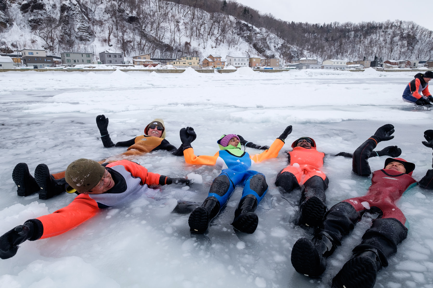 A group of travellers float in the frozen Sea of Okhotsk while wearing bright coloured dry suites
