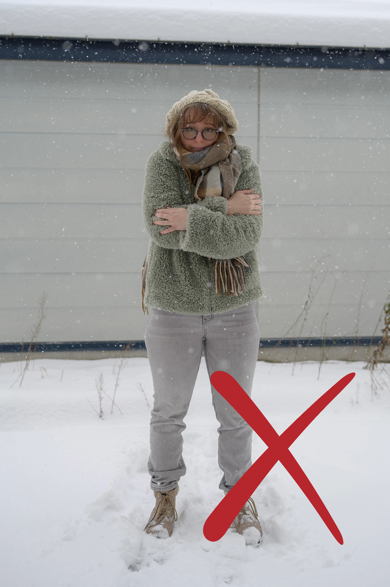 A girl with glasses stands in the snow shivering. She is wearing jeans, low-cut boots and a fuzzy teddy bear jacket, all of which don't appear to be suitable for the cold.