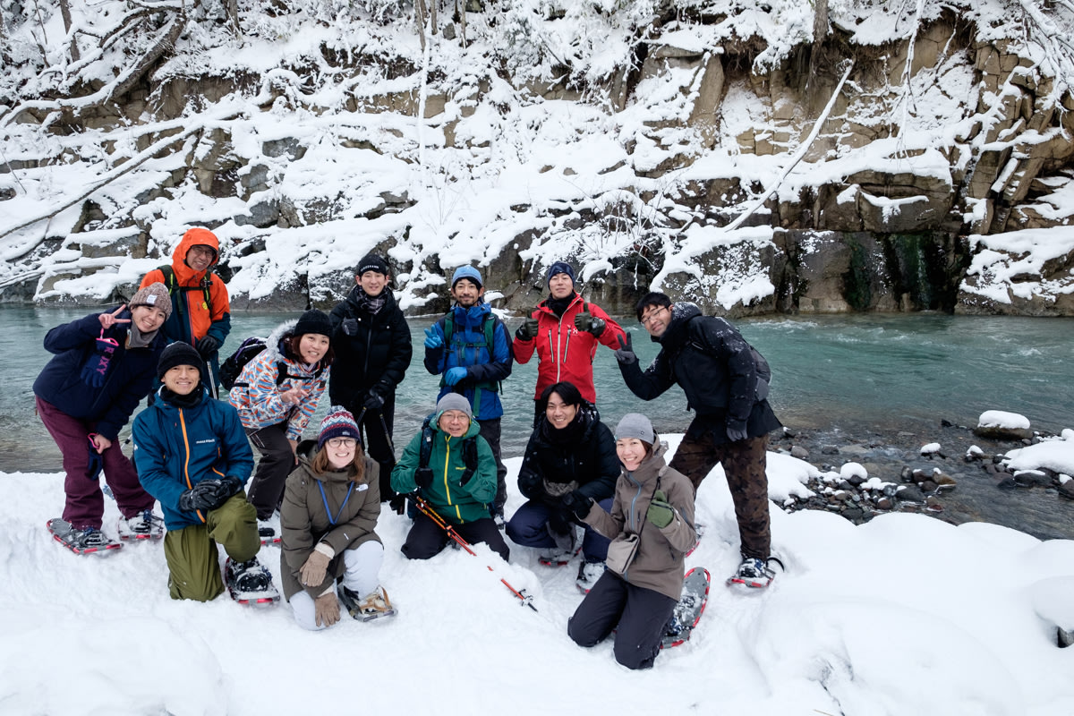 A group photo at Biei's Blue River. A group of people crouch in front of the river, smiling at the camera.
