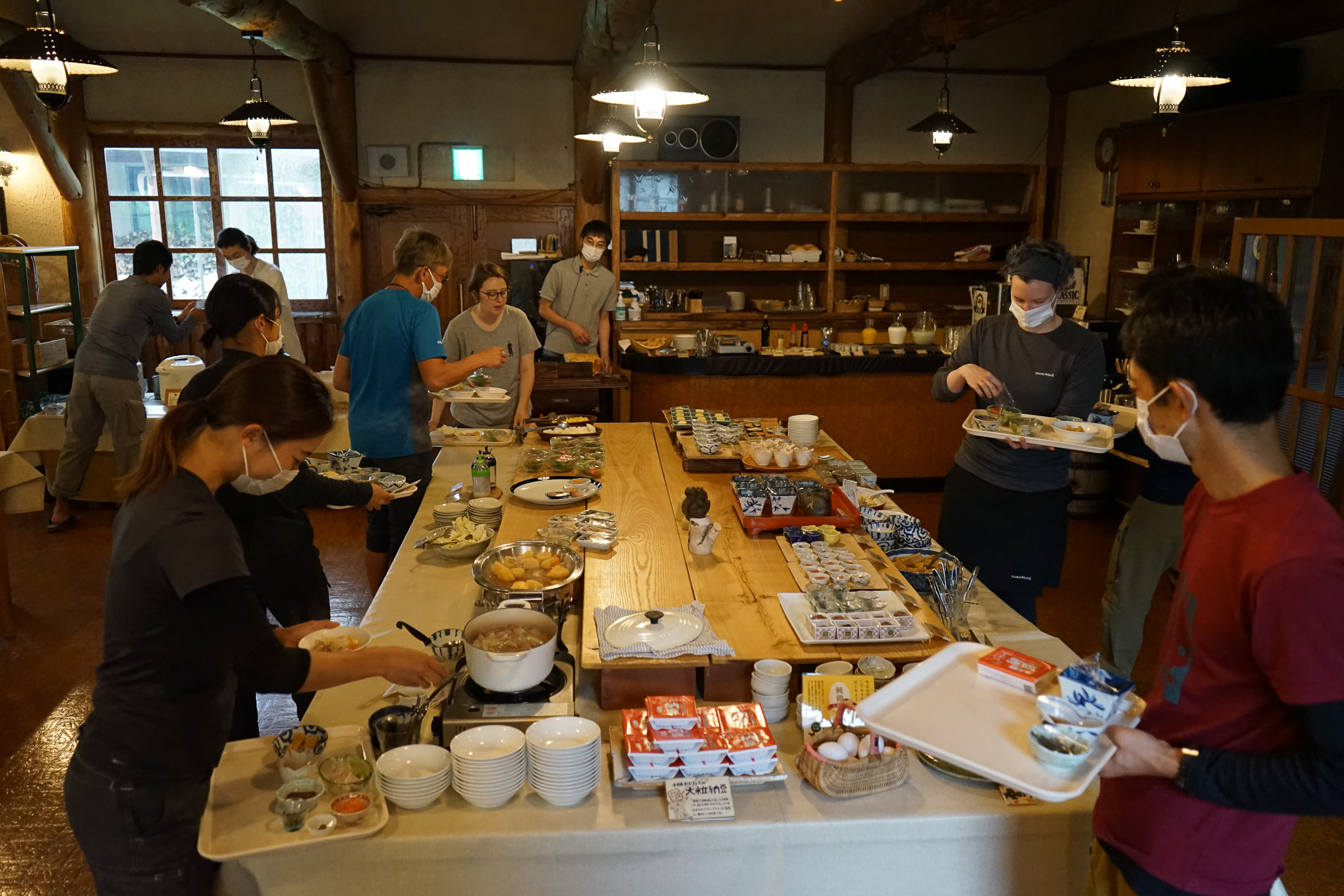 Adventure Hokkaido guides and guests gather around a breakfast buffet, choosing food to eat for breakfast.