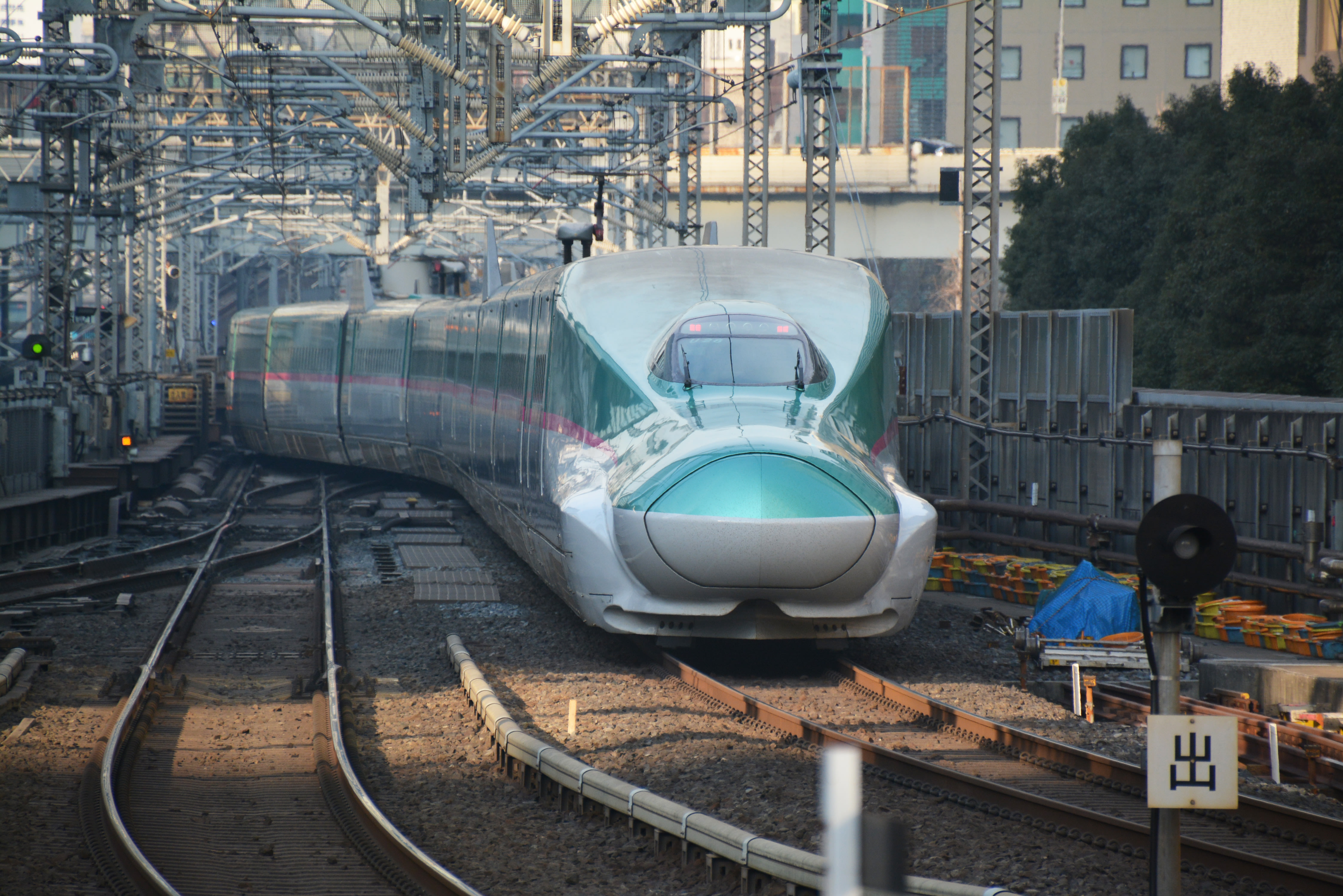 The green Hokkaido Shinkansen, a large, high-speed train, rounds a corner on train tracks in Tokyo. 