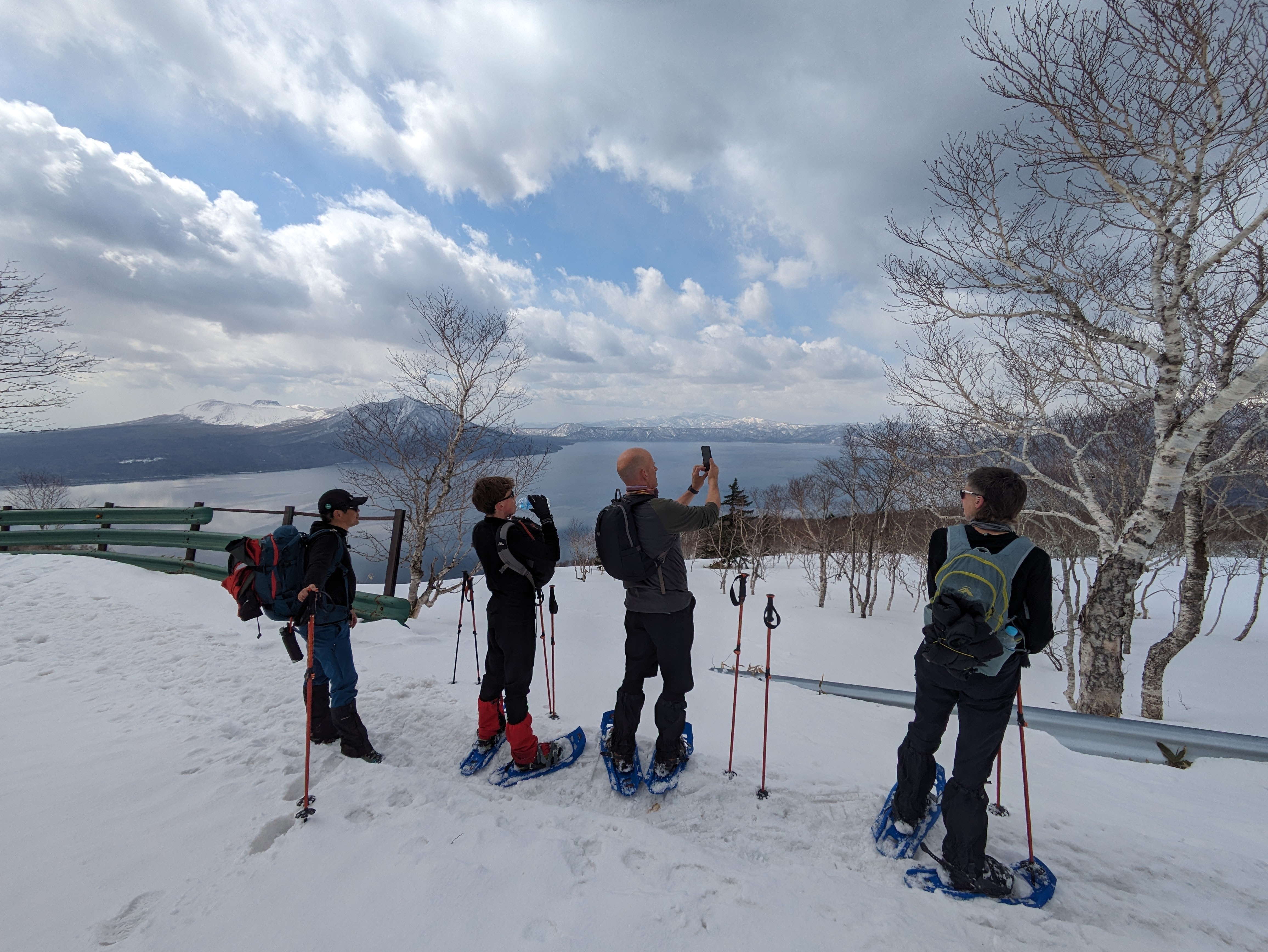 Guests take pictures of the birch trees by Lake Shikotsu while snowshoeing up Mt. Monbetsu.