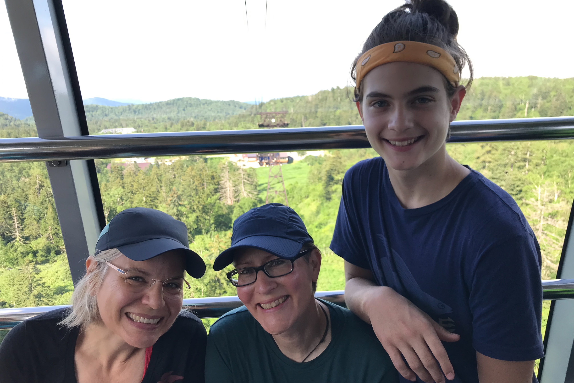 A family of two ladies and a teenage girl smile at the camera. They are riding in a ropeway cart.